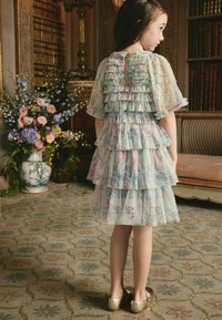 Világoszöld virágos ruha réteges fodrokkal, áttetsző ujjakkal és kulcslyuk alakú hátkivágással. Arany balettcipővel párosítva.