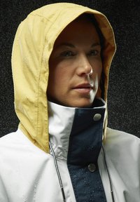 Giacca impermeabile con cappuccio giallo, corpo bianco e dettagli blu navy. Tessuto testurizzato con gocce d'acqua visibili e zip di chiusura.