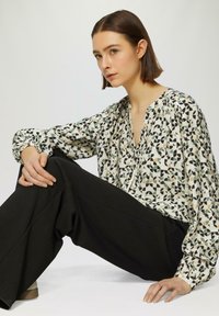 Blouse à manches longues présentant un motif géométrique abstrait en noir, crème, vert et beige, associée à un pantalon large taille haute noir.