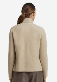 Beige tekstureret sweater med høj krave og lange ærmer. Designet har en ribbet struktur og en lige kant.