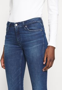 Mörkblå skinny jeans i denim med hög midja, fem fickor och silverdetaljer samt en slät textur.