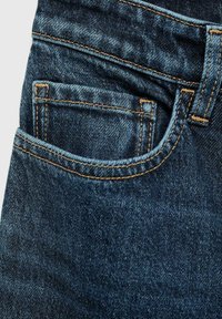 Granatowe dżinsy typu slim fit z przednią kieszenią, widocznym ściegiem w kontrastującym jasnobrązowym kolorze oraz miękkim, teksturowanym wykończeniem.