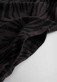 Gros plan sur un tissu doux et sombre avec des rayures zèbre noires subtiles, drapé sur une surface blanche.