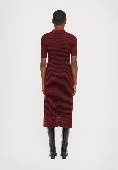 Knee-length, burgundy striped dress with short sleeves and a polo collar, made of textured knit fabric. Worn with black knee-high boots.