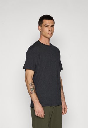 Dunkelgraues Baumwoll-T-Shirt mit kurzen Ärmeln, Rundhalsausschnitt und einer dezenten Brustbestickung; kombiniert mit locker sitzenden grünen Hosen.
