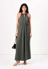 Vestido maxi em verde-azeitona, sem mangas, com decote em gota, cintura elástica e tecido suave, combinado com sandálias nudes de tiras e uma bolsa preta.