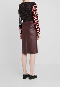 Jupe crayon en cuir bordeaux à coupe ajustée. Haut à manches longues avec un motif mélangé d'imprimés léopard et serpent. Chaussures plates noires.