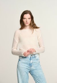 Maglione leggero, lavorato a maglia, di colore bianco sporco, con maniche lunghe e scollo a barca, abbinato a jeans in denim blu sbiadito con vita alta.