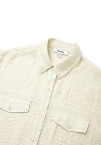 Camicia abbottonata in crema chiaro, tessuto testurizzato. Presenta un colletto, due tasche frontali e chiusura a bottoni. Design resistente con dettagli minimali.