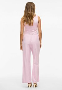 Un haut sans manches rose associé à un pantalon large rose clair. Le tissu semble lisse avec une taille élastique. Les chaussures possèdent un design à talon haut.