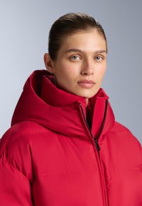 Piros steppelt dzseki magas gallérral és nagy kapucnival. Elől cipzáras, sima, fényes felületű, hideg időre alkalmas.