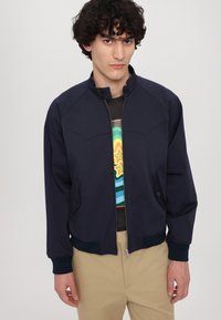 Giacca bomber blu navy in materiale leggero con chiusura a zip, colletto a scatto, tasche laterali e polsini a coste. Presenta un design pulito e strutturato.
