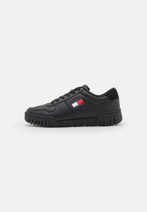 Czarny, niskoprofilowy sneaker z grubą podeszwą i sznurowadłami, z małym prostokątnym logo z czerwonymi, białymi i niebieskimi paskami po boku.
