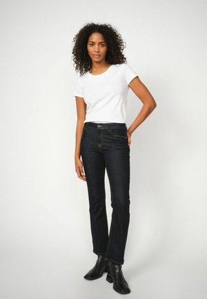 Tumši zili džinsa džinsi ar taisnu griezumu, dzeltenām šuvēm, pogas aizdari un gludu faktūru. Kopā ar baltu T-kreklu.