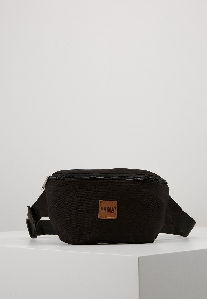 Sac banane en tissu noir avec fermeture éclair et sangle réglable, orné d'un patch logo "Urban Classics" marron à l'avant.