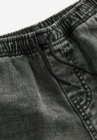 Los joggers de mezclilla negra cuentan con una cintura elástica con cordón ajustable. La textura es ligeramente desgastada con detalles de costura en contraste.