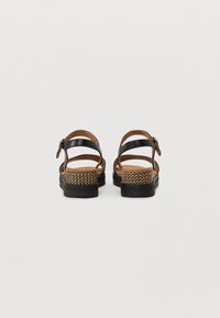Sandales noires en cuir avec un accent en fibre naturelle tissée sur le talon, dotées d'une sangle ajustable et d'une semelle plate en caoutchouc.