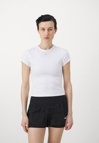 Weißes, figurbetontes Kurzarmshirt kombiniert mit schwarzen Sportshorts mit Plissee-Design und kleinem weißem Logo an der Seite.