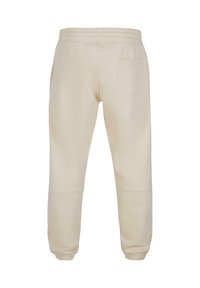 Beige joggebukser med elastisk midje og mansjetter, med en enkelt baklomme og en glatt tekstur.