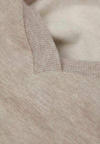 Lichtbeige trui met een gestructureerde, ribbelige halslijn. De stof lijkt zacht met subtiele kleurvariaties en een gladde afwerking.