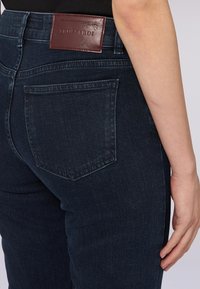 Tmavé denimové džíny s přiléhavým střihem, které mají koženou nášivku na pase a decentní design zadní kapsy.