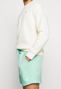 Sweatshirt crème avec des poignets et un col côtelés, associé à un short vert menthe clair avec une taille élastique et des poches latérales, logo Nike visible.