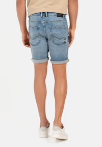 Denim shorts met een lichtblauwe was, omgeslagen cuffs en twee achterzakken. Bevat gele stiksels en een logo patch op de tailleband.