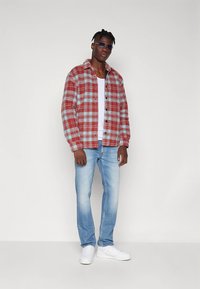 Camicia di flanella a quadri rossi e blu, T-shirt bianca sotto, jeans azzurri chiari e sneakers bianche, con occhiali da sole incorniciando il volto.