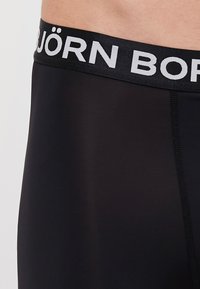 Μαύρο εσώρουχο με φαρδιά ελαστική ζώνη που φέρει τυπωμένο το "BJÖRN BORN" σε λευκό. Λείο υλικό και εφαρμοστό σχέδιο.