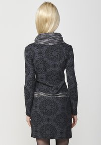 Schwarz gemustertes Kleid mit hohem Kragen, aufwendigen Designs, strukturiertem Stoff und einem silbernen Taillendetail. Lange Ärmel und eine figurbetonte Silhouette.