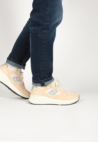 Cream and light orange athletic sneakers with mesh and suede upper, white midsole, and gray accents, paired with rolled dark blue jeans.