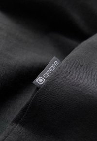 Černá látka s žebrovanou strukturou, s malou šedou štítkem s nápisem "ombre" přišitým do švu.