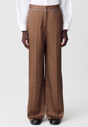 Pantalon marron à motifs avec une jambe large et un accent bleu à la taille. Le tissu présente un imprimé géométrique avec de petits cercles.