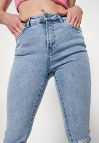 Jeans de cintura alta em azul claro, feitos de denim, com um design clássico de cinco bolsos e um leve desbotamento, apresentando um detalhe desgastado na bainha.