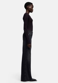 Zwarte jeans met hoge taille en rechte pijpen, voorzien van vijf zakken, subtiele vervaging en een gladde textuur. Gecombineerd met een top met lange mouwen.