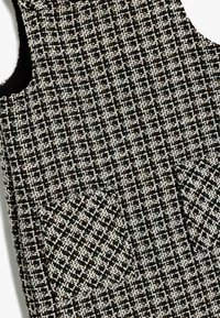 Schwarz-weiß gewebtes Kleid aus strukturiertem Stoff mit Karomuster. Enthält zwei Vordertaschen mit spitzen Ecken.