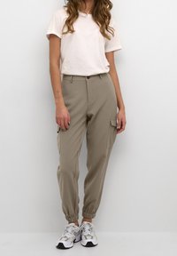 Ljusbeige cargobyxor med elastiska mudd, sidofickor och knäppning, tillsammans med en enkel vit t-shirt och vita sneakers.