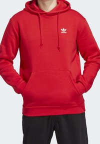 Röd hoodie gjord av mjukt tyg med en känguruficka, dragskoä hood och en liten vit Adidas-logotyp på bröstet.