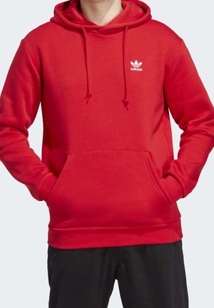 Červená mikina s kapucí vyrobená z měkké tkaniny, s klokanní kapsou, kapucí na šňůrku a malým bílým logem Adidas na hrudi.
