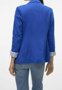 Niebieska marynarka o strukturalnym kroju, z wyciętym kołnierzem i podwiniętymi mankietami w paski. Teksturowana tkanina, zaprojektowana z myślą o dopasowanym fasonie.
