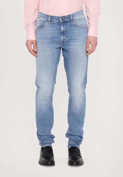 Light blue denim jeans with a slim fit, faded texture, five pockets, and a button closure. Styled with a pink shirt and black shoes.