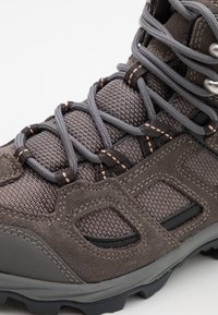 Gray outdoor boot with textured fabric, grey laces, and black rubber sole. Features reinforced eyelets and cut-out details on the side.