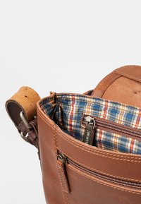 Borsa a spalla in pelle marrone con finitura testurizzata, dotata di un interno foderato a quadri e numerose tasche con zip.