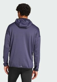 Pull-over de sport violet avec capuche, doté de manches longues, d'un tissu texturé et d'un cordon de serrage. Inclut un logo sur l'ourlet.