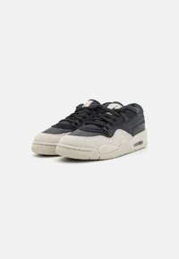 Zapatillas con parte superior de cuero negro, puntera de gamuza gris y suela de goma blanca. Cuenta con un collar acolchado, cordones y una unidad de aire visible en el talón.