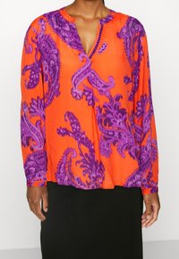 Blusa a maniche lunghe in tessuto arancione brillante, caratterizzata da intricati motivi paisley viola, scollatura a V con cuciture decorative e una vestibilità comoda.
