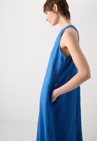 Ärmlös klänning i knälängd gjord av lätt blå linne, med en avslappnad silhuett, sidofickor och en något texturerad yta.