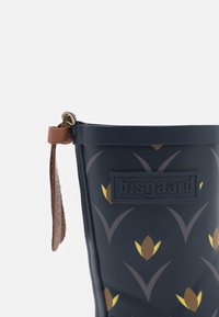Botte de pluie en caoutchouc marine avec un motif floral jaune et marron, sangle d'accent en cuir et logo en relief sur le côté. Texture lisse sur toute la surface.