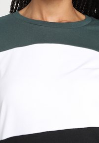T-shirt in misto cotone con collo rotondo, design color-block in verde scuro, bianco e nero, con una texture liscia.