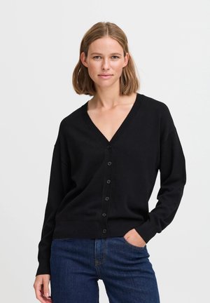 Cardigan nero realizzato in morbido tessuto, caratterizzato da scollo a V, maniche lunghe e chiusura a bottoni. Indossato sopra jeans blu, con texture liscia.
